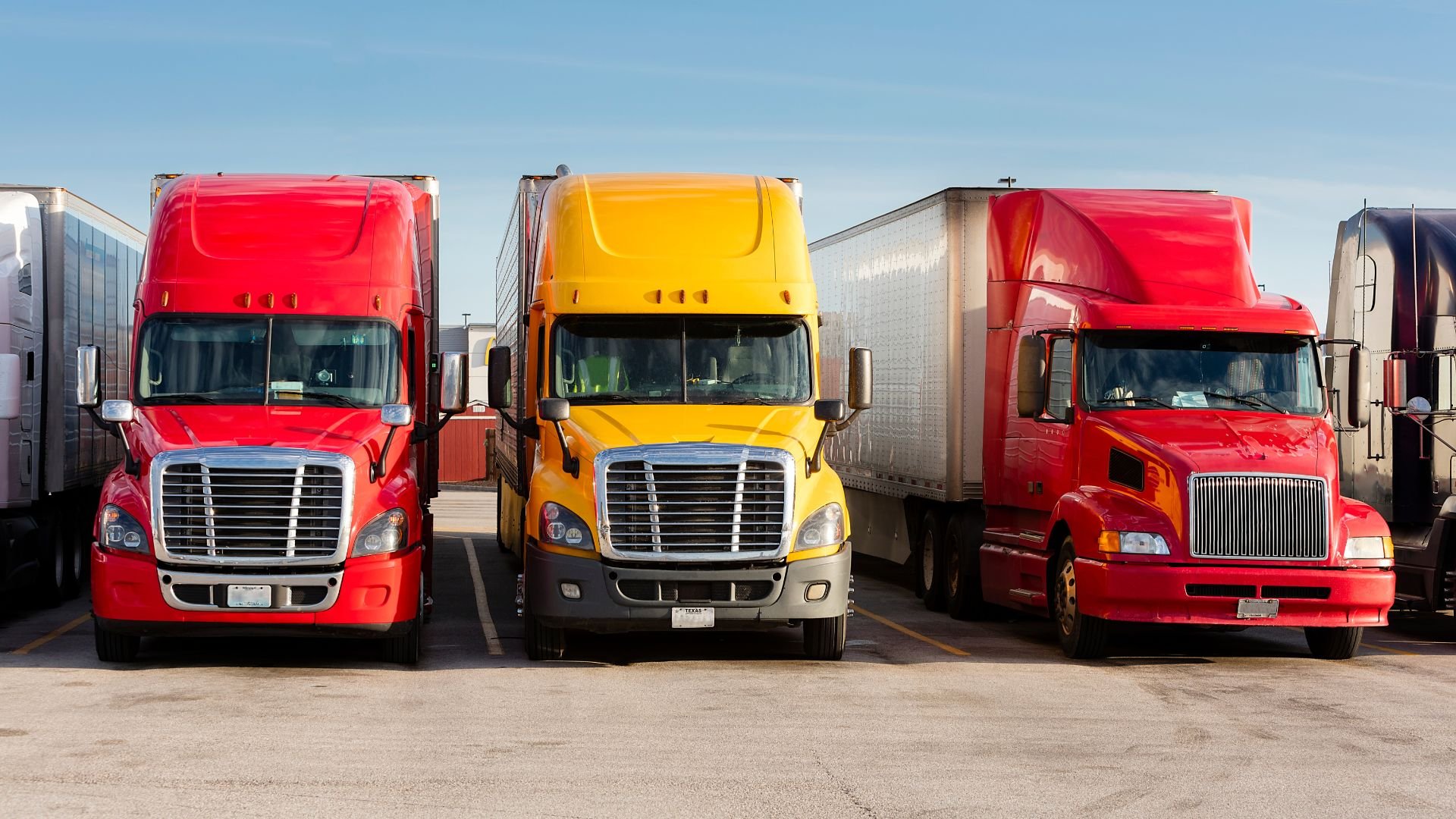 Three semi-trucks in red and yellow parked in a truck parking lot