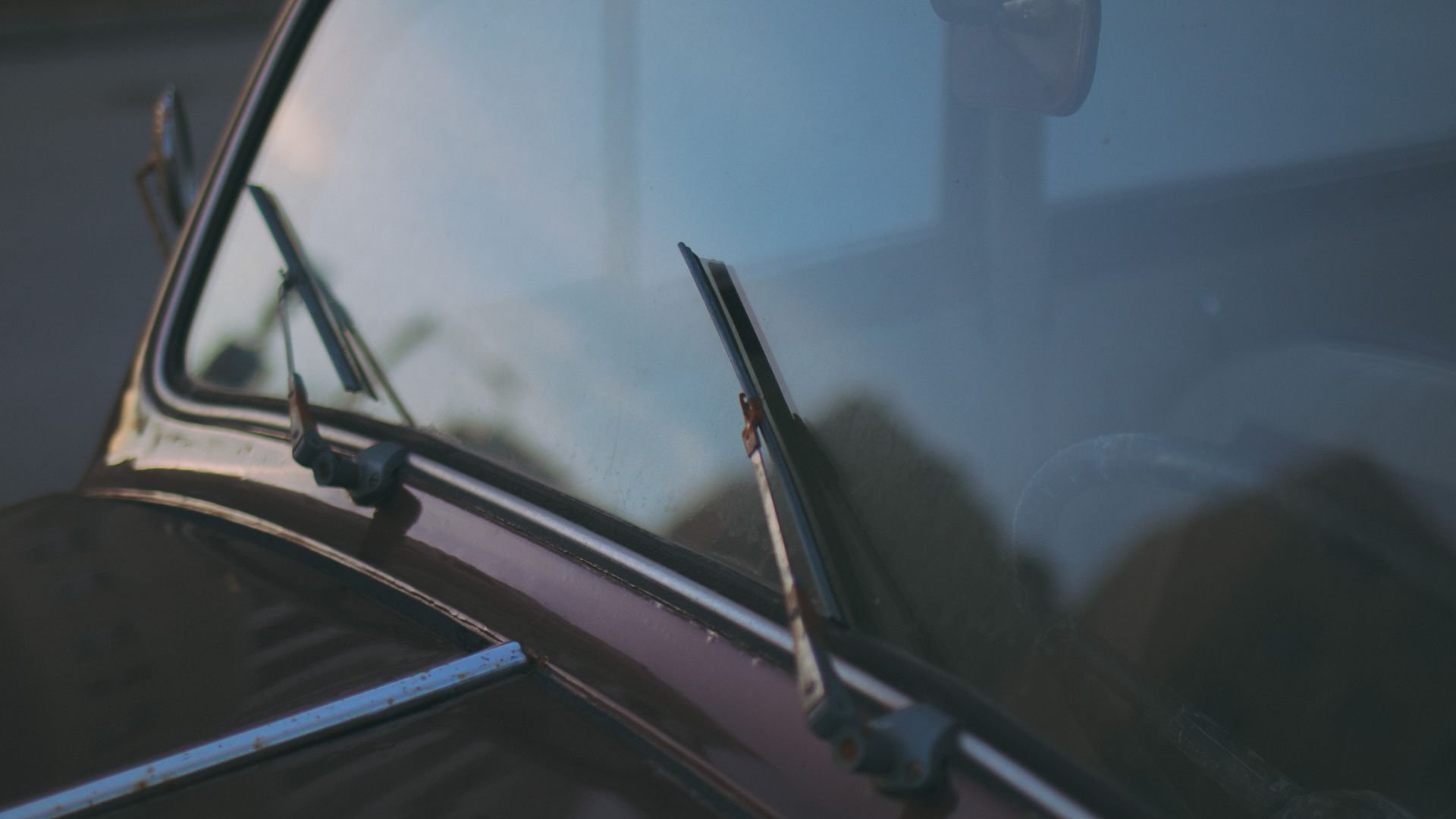 Windshield wipers on a car window with blurry outdoor background