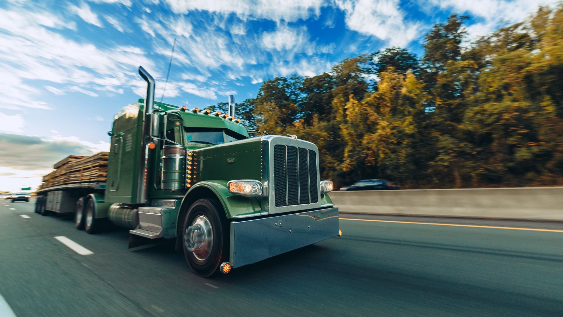 Green semi-truck hauling lumber travels down highway on sunny day