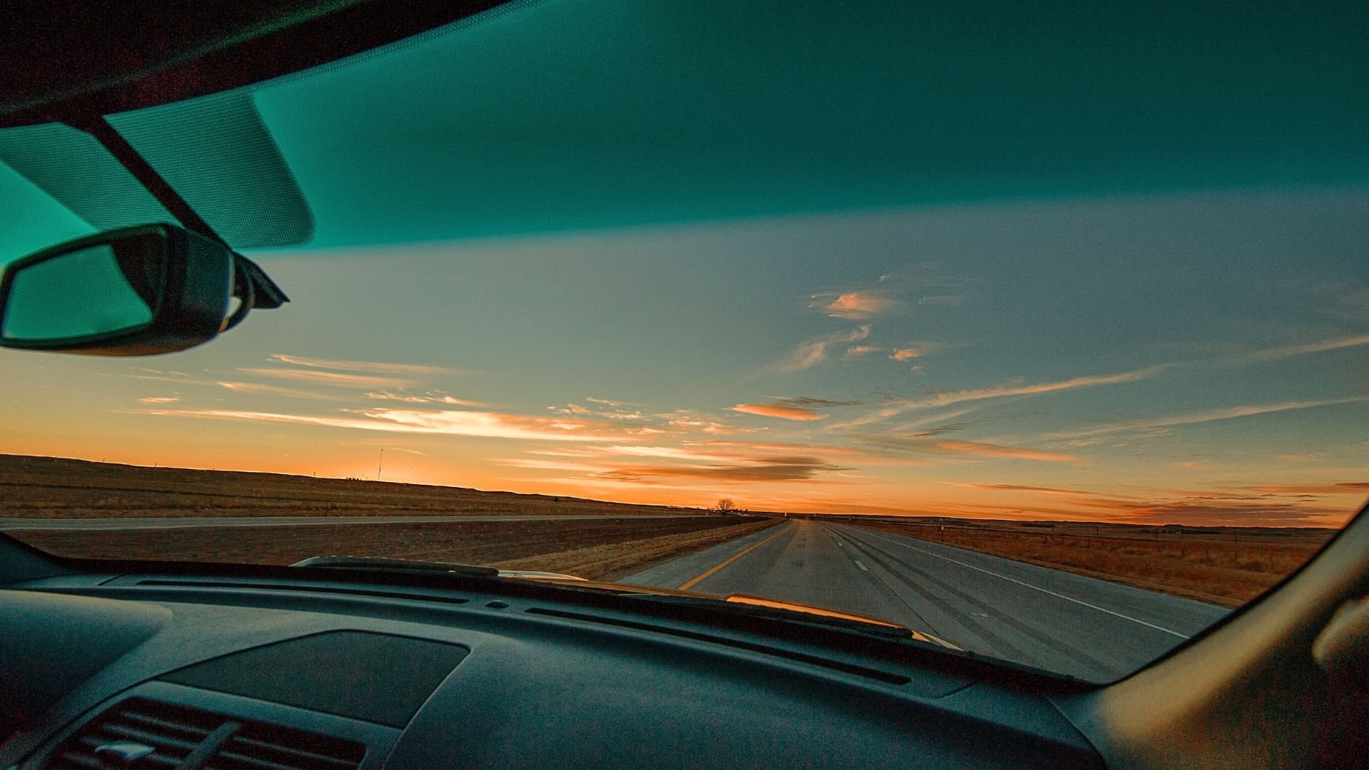 Open road at sunset, viewed through car windshield, empty highway ahead