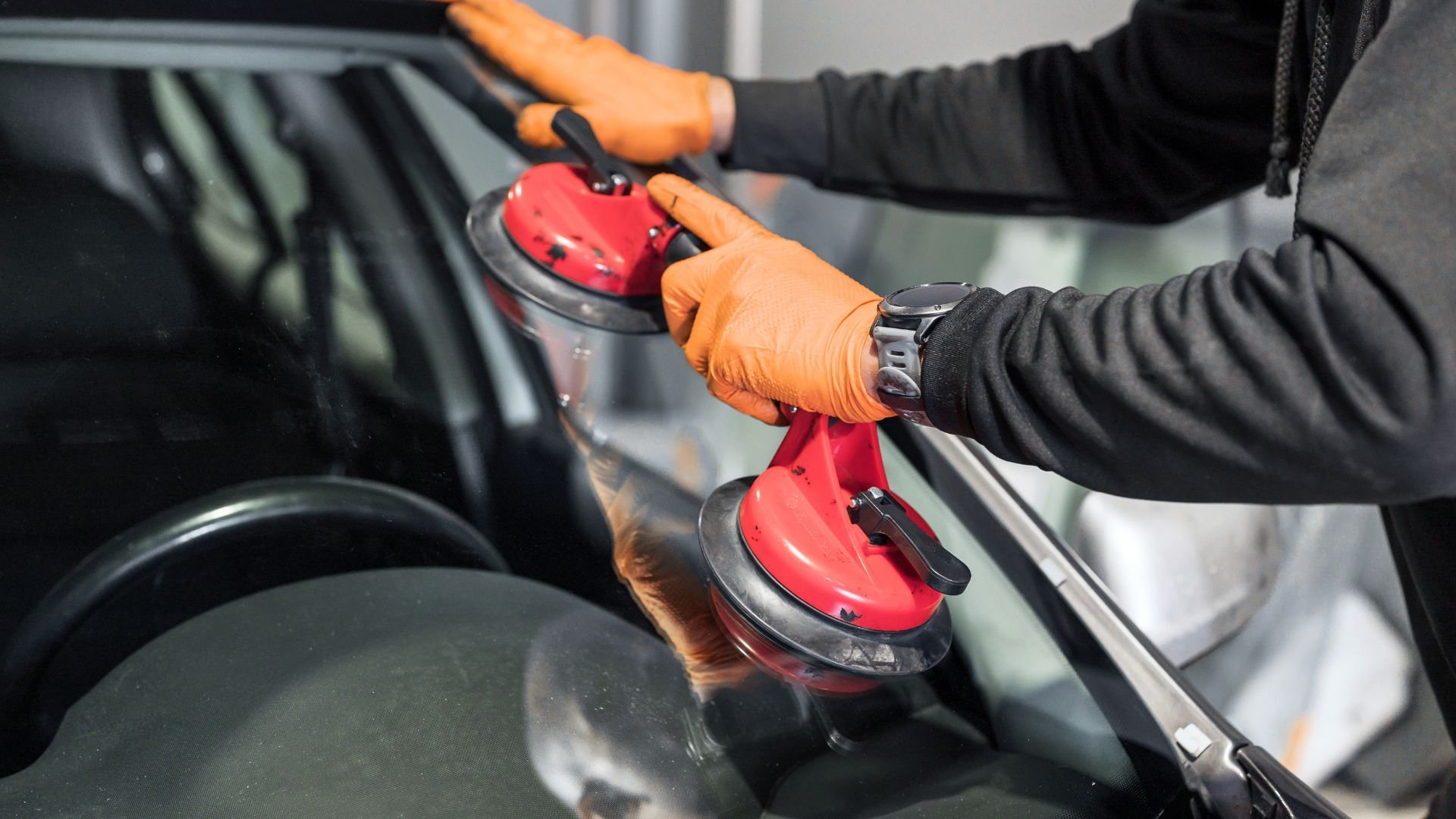 Hands in orange gloves using red suction cups to install car windshield