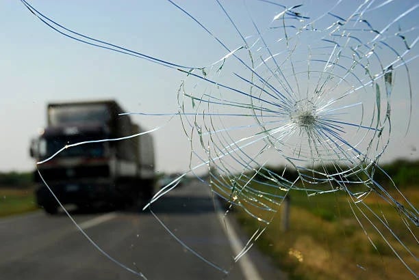 Cracked windshield with truck in background on rural highway