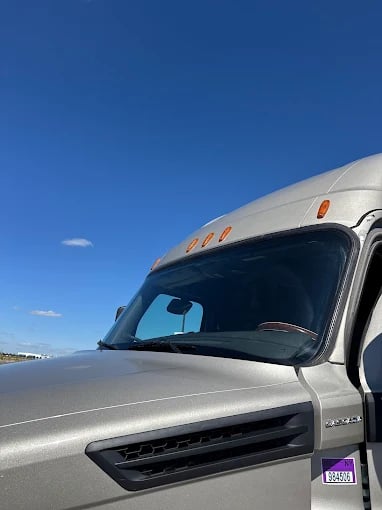 Silver semi-truck cab against bright blue sky with side marker lights